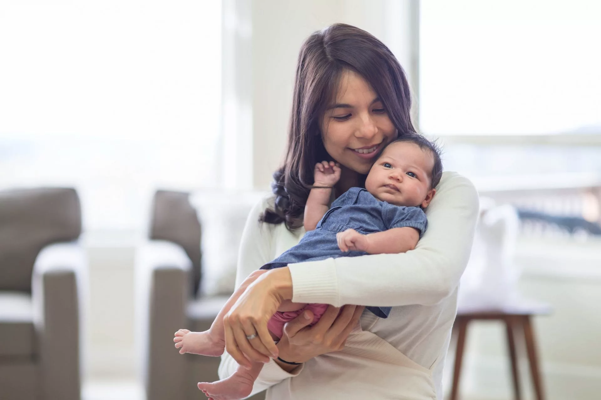 Mom holds her newborn daughter with tenderness and love. The baby is looking at something on the ceiling...