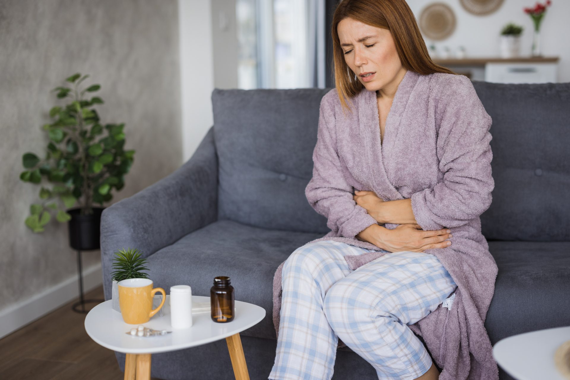Woman suffering from abdominal pain while sitting on sofa at home