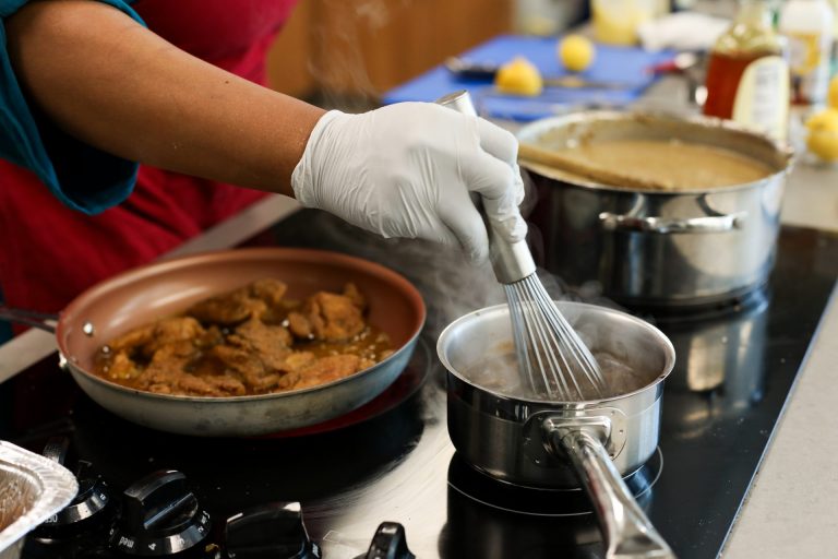 Chef at a cooking demo stirring sauce in a pot while frying chicken in a pan