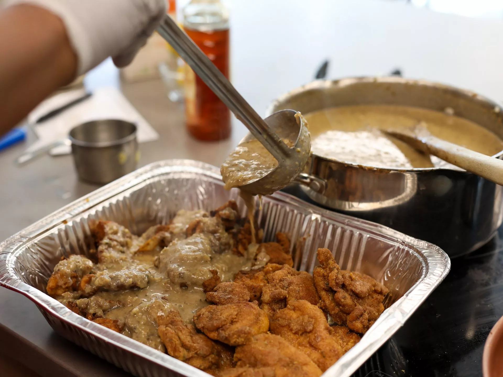 Chicken in a pan being covered by a sauce in a ladle