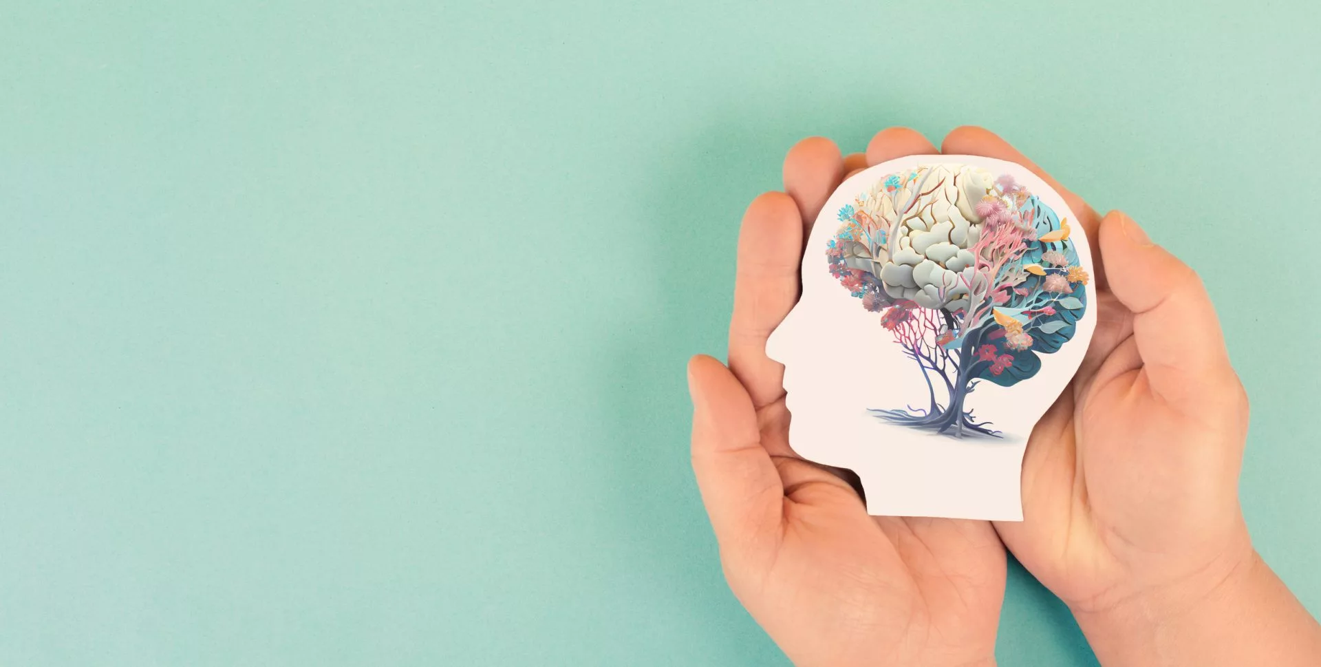 Hands holding paper head, human brain with flowers, self-care and mental health concept.