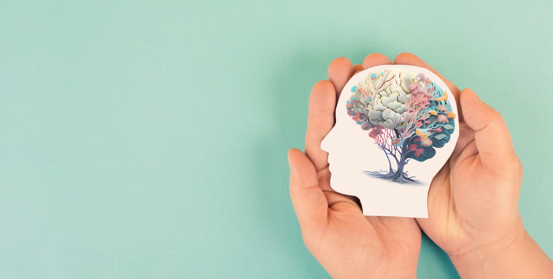 Hands holding paper head, human brain with flowers, self-care and mental health concept.