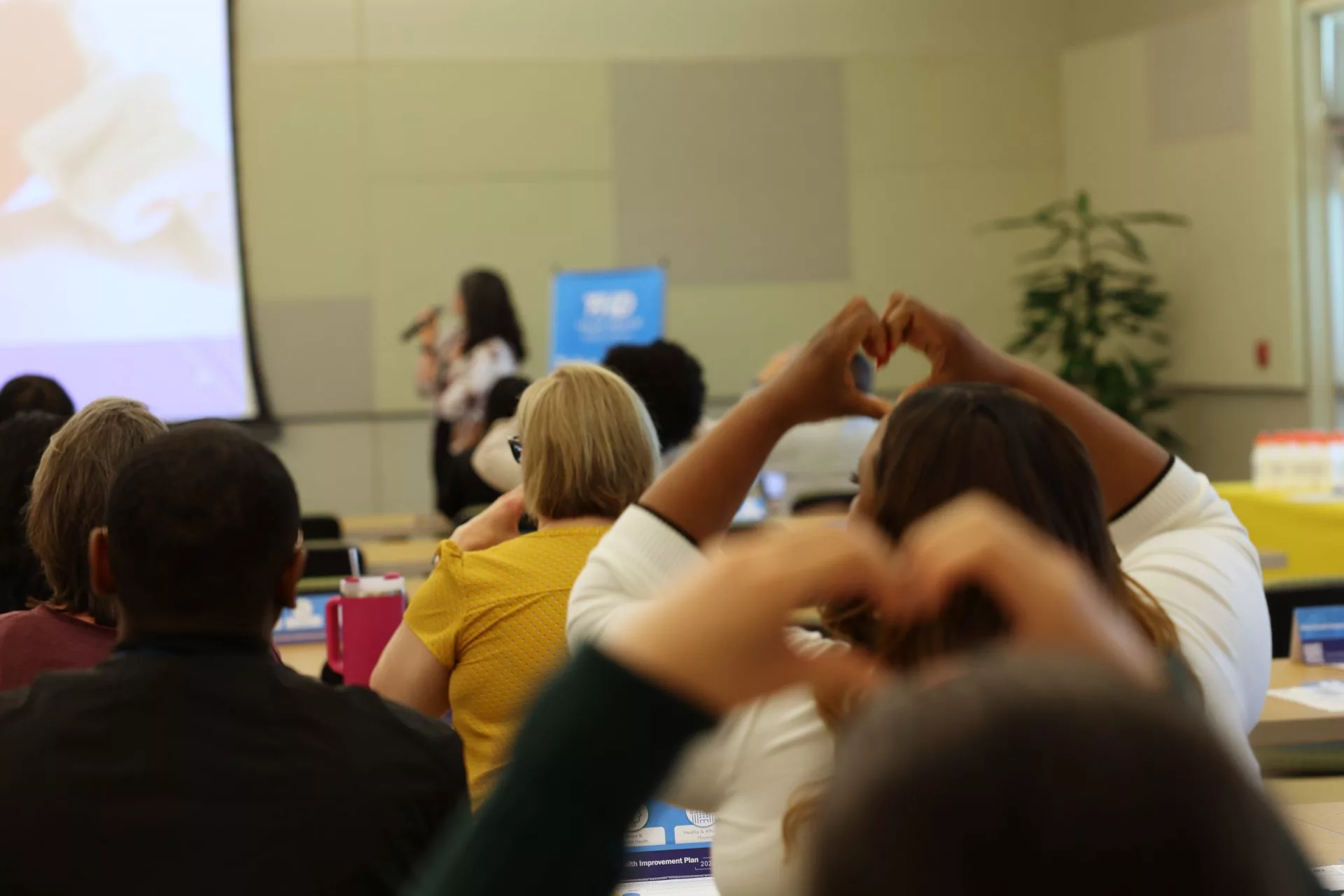Room listening to presenter and lifting hands up in a heart gesture