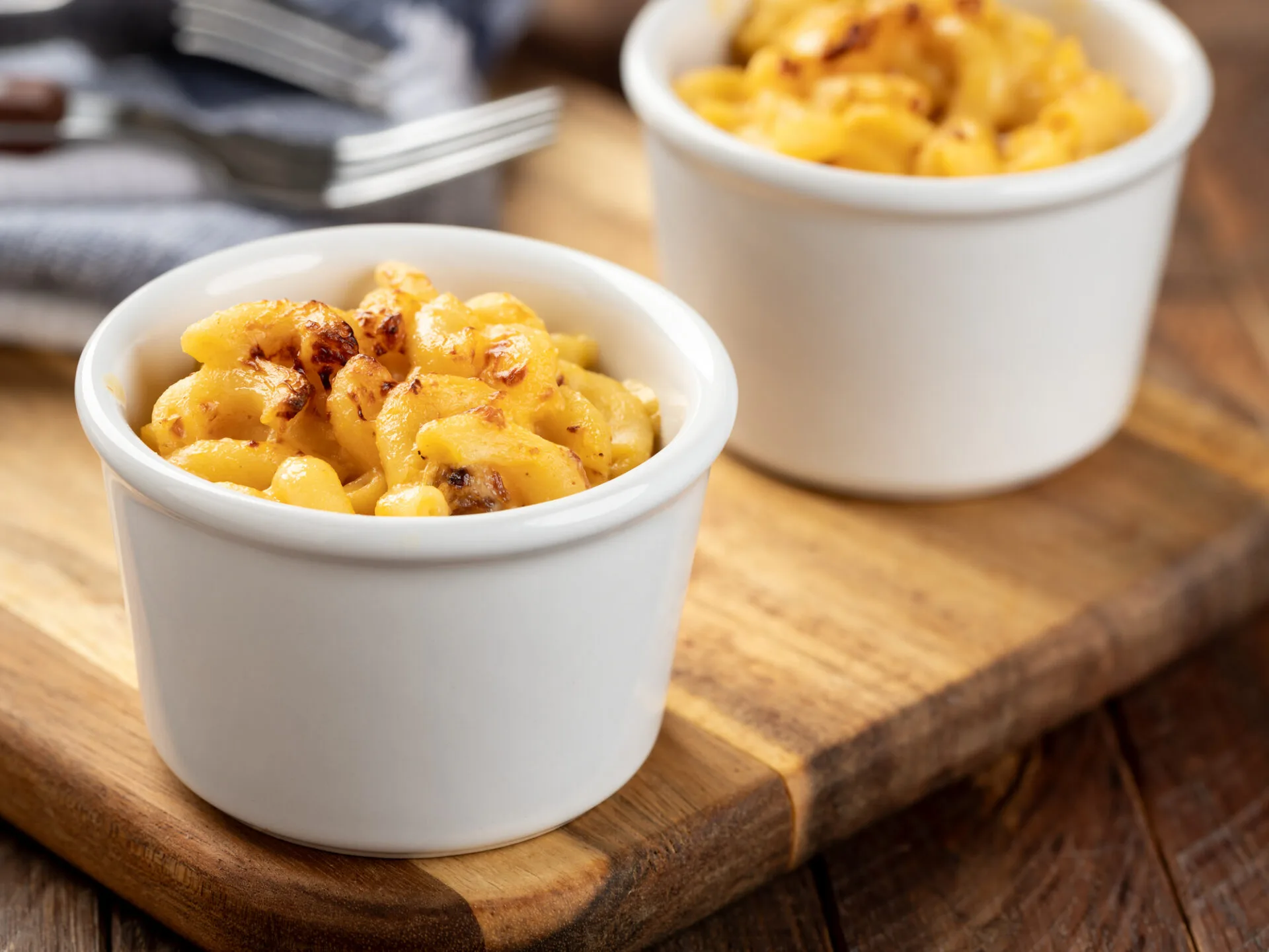Baked macaroni and cheese in a white cup on a wooden board