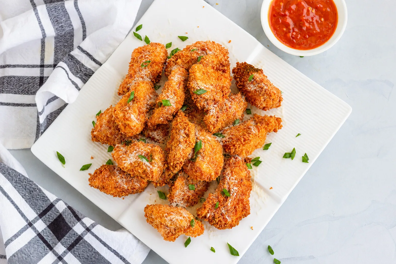 Chicken parmesan bites on a white plate with marinara sauce in a cup next to it